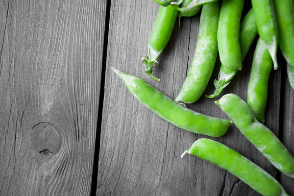 On a wooden background are green pea pods on the side. On the right there are a lot of green peas, on the left - a wooden background. Photo with green peas.