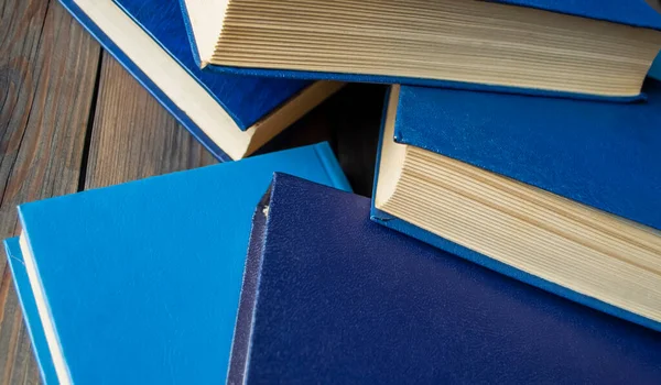 Lots of books with a blue cover on a wooden table. Scattered randomly books with a blue paliture.