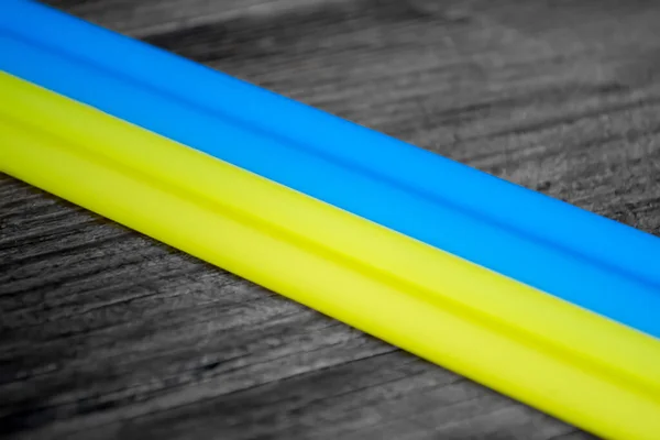 On a gray, turf background lie blue and yellow tubes together. Yellow-blue flag of Ukraine with tubes on a wooden background. Two stripes of the flag - blue and yellow, like the flag of Ukraine.