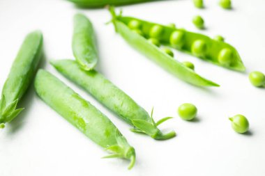 Beyaz arka planda yeşil bezelyelerden oluşan açık bir kabuk var ve onun yanında kapalı duruyor. Kapsülün içinde yeşil bir sıra fasulye. Beyaz arkaplandaki bir modülde fasulye.