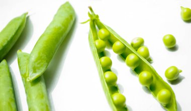 Beyaz arka planda yeşil bezelyelerden oluşan açık bir kabuk var ve onun yanında kapalı duruyor. Kapsülün içinde yeşil bir sıra fasulye. Beyaz arkaplandaki bir modülde fasulye.