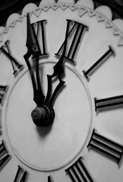 The clock shows without five minutes twelve. Hands of the clock at 11:55. Roman chickens. Carved arrows. Openwork hands on the clock. Old clock.