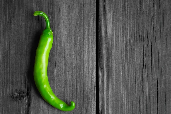 Green, hot pepper on the gray background of the tree. gray wood and green chili pepper. The contrast of the green vegetable on the gray tree. Chili pepper. Green pepper pod.