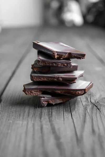 Vertical photo - chocolate stacked on a wooden table. On a wooden table is a stack of chocolate. pieces of chocolate lie in the tower.