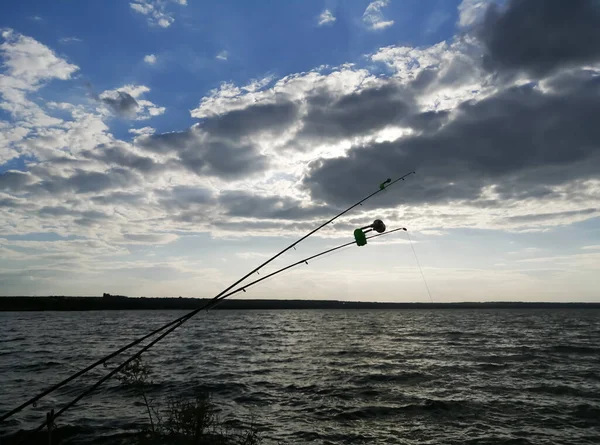 Two fishing rods are thrown into the river. Fishing rods with bells against the background of the river and cloudy sky. Beautiful sky, river and two close-up fishing rods.