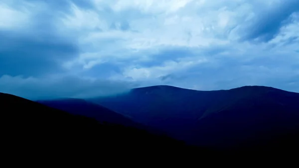 Dramatic sky in blue-gray tones over the mountains. Dark mountains and stormy skies are black and blue. Almost black mountains and blue-gray, cloudy skies. Stormy skies over the mountains.