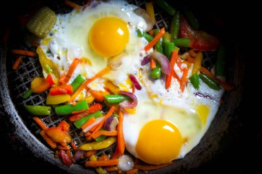 Healthy breakfast fried eggs with vegetables in a frying pan. view from above. Dark background top view.