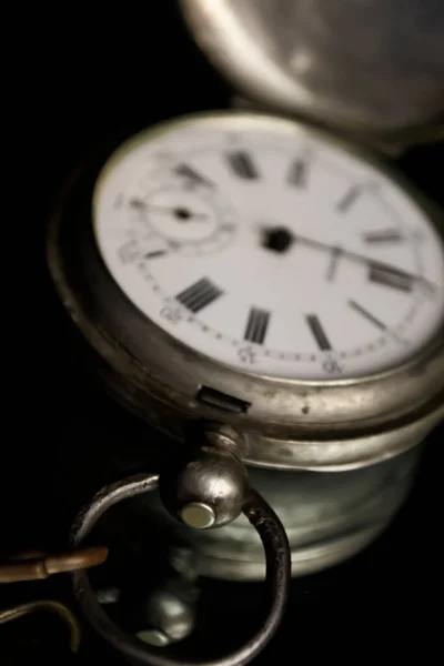 An old clock on a dark background. Mirrored background and pocket watch. A watch with one hand. Shifted focus.