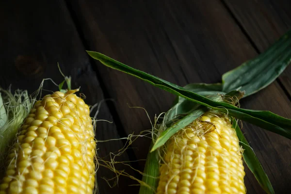 In the lower right corner of the photo is a lot of corn close-up. corn of the Raquel variety, sweet, with yellow-white grains on a wooden table.