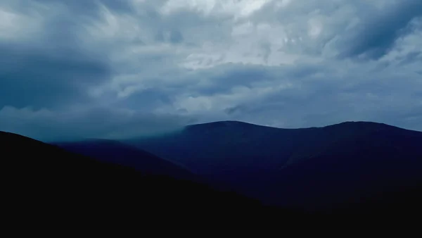 Dramatic sky in blue-gray tones over the mountains. Dark mountains and stormy skies are black and blue. Almost black mountains and blue-gray, cloudy skies. Stormy skies over the mountains.