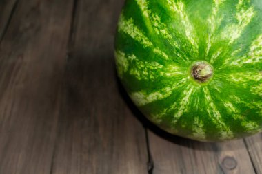 Part of the watermelon is visible when macro-photographed on the table. On the wooden table you can see part of a large green watermelon, a close shot.