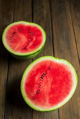 two halves of watermelon lie on a wooden table. On the table are two halves of red, ripe watermelon.