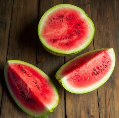 There is a watermelon on a wooden table. half and two quarters of watermelon are on the table. WOODEN-based red, ripe watermelon.