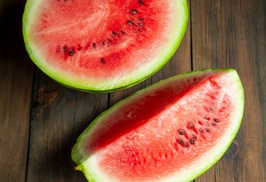 On a wooden table are slices of watermelon. Watermelon quarters on a wooden base. Watermelon season, big. sweet berries.