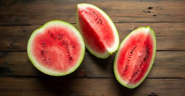 There is a watermelon on a wooden table. half and two quarters of watermelon are on the table. WOODEN-based red, ripe watermelon.