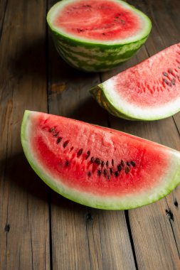 There is a watermelon on a wooden table. WOODEN-based red, ripe watermelon. half and two quarters of watermelon are on the table. Vertical photo
