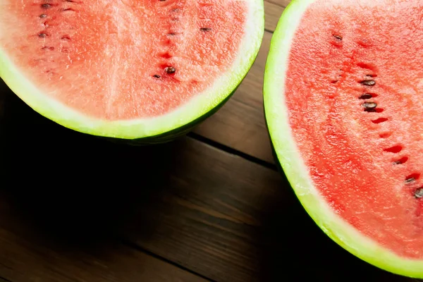 Two halves of watermelon lie on a wooden table. A close shot of a watermelon - parts of two halves with a red crumple of watermelon on a wooden table.