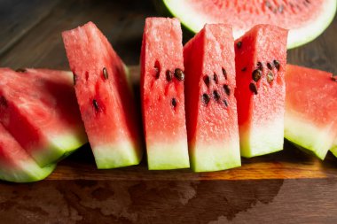 Watermelon cut into small triangles on a wooden board. On a wooden table is a board with slices of watermelon. Sweet slices of watermelon with bones.