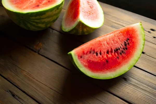 There is a watermelon on a wooden table. half and two quarters of watermelon are on the table. WOODEN-based red, ripe watermelon.