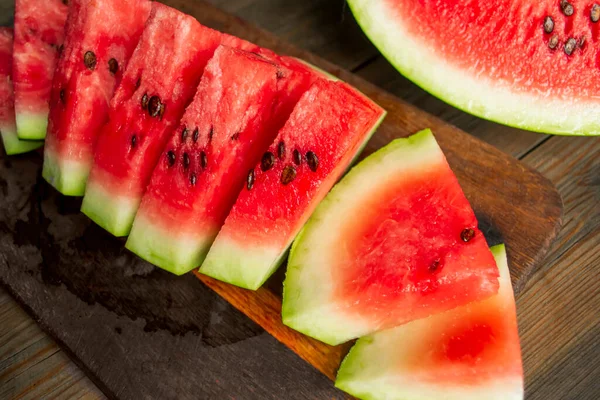 Watermelon cut into small triangles on a wooden board. On a wooden table is a board with slices of watermelon. Sweet slices of watermelon with bones.