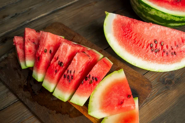 Watermelon cut into small triangles on a wooden board. On a wooden table is a board with slices of watermelon. Sweet slices of watermelon with bones.
