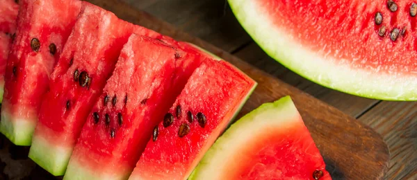 Watermelon cut into small triangles on a wooden board. On a wooden table is a board with slices of watermelon. Sweet slices of watermelon with bones.