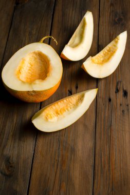 Vertical photo. Melon lunch is vegetarian. On a wooden table lies half a melon and three slices. peeled melon, without seeds on the table.