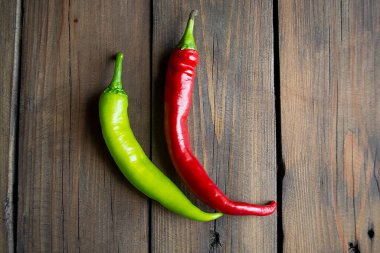 On a wooden table are two pods of hot peppers, red and green. Two pods sharp. Hot peppers of green and red colors on a wooden background.