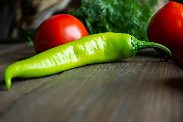 On the wooden table is green peppers. hot pepper green zuvette on the table with other vegetables. A green hot pepper pod lies on a wooden table among other vegetables.
