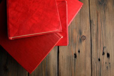 Red books are thrown on the table. books with a red cover lie on a wooden table. A bunch of books with a scarlet cover on a wooden table.