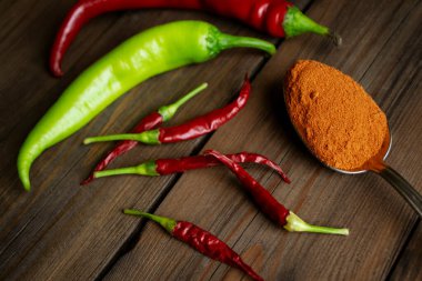 Red and green hot peppers on the table and chopped chili peppers in a spoon. Pepper powder in a spoon next to fresh chili peppers. Wooden background.