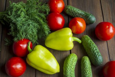 On the table are red tomatoes, cucumbers and fresh dill. the vegetables on the salad lie together. Summer vegetables from the garden - peppers, tomatoes and cucumbers with dill.