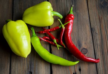 Different types of pepper on the table. On a wooden table are two bell peppers, a hot green pepper, a hot red pepper and a lot of small chilies.