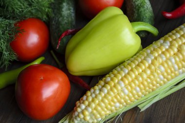 On the table are tomatoes, corn, cucumbers, dill, hot peppers, sweet peppers. Different vegetables from the garden lie together. Useful vegetables on the table.