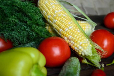 On the table are tomatoes, corn, cucumbers, dill, hot peppers, sweet peppers. Different vegetables from the garden lie together. Useful vegetables on the table.