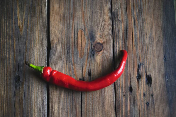 Thin chili pepper on a wooden table. Red pepper on a wooden background. One hot pepper on the table. Beautiful hot pepper.