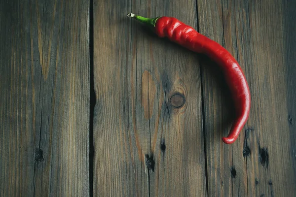 Red pepper on a wooden table. Red thin pepper lies on a wooden background. One red hot pepper.