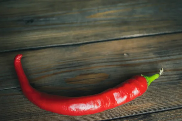 Red pepper on a wooden table. One red hot pepper. Red thin pepper lies on a wooden background.