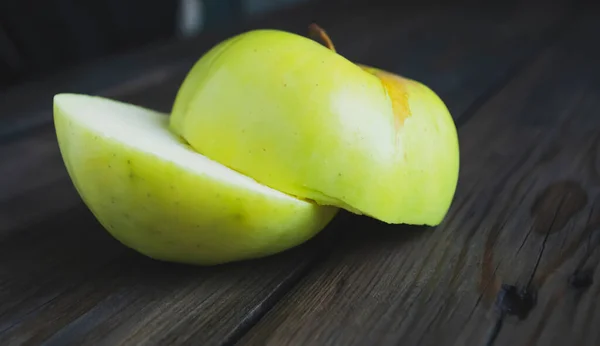 Two halves of a green apple on a wooden table. The cut apple is green. On the table are two halves of an apple.