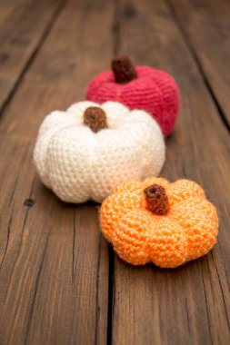 Üç balkabağı ahşap bir masanın üzerinde duruyor. Ahşap bir masanın üzerinde, örülmüş balkabakları sıraya dizilir. Turuncu. Beyaz ve kırmızı iplik Tyva, kendi ellerinle. Cadılar Bayramı için sonbahar süslemeleri.