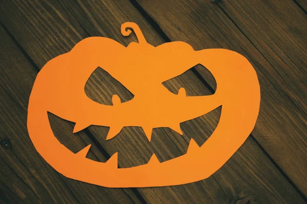 A jack lantern made of orange paper on a wooden table. Halloween crafts. Carved pumpkin for Halloween. A terrible pumpkin on the holiday of Samhain.