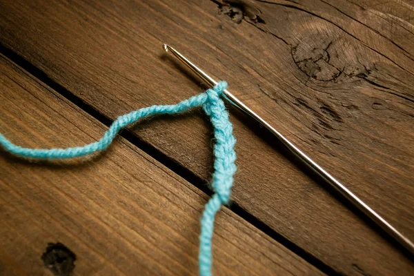 フック上の列の空気ループ かぎ針編みだ ループの最初の行はクロッキーされます 青い糸で交差してる 木製のテーブルの上に編み物でフック — ストック写真