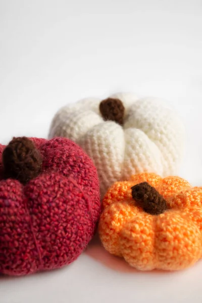 On a white background there are three crocheted pumpkins. White, orange and red pumpkins crocheted. the autumn scenery is pumpkins.