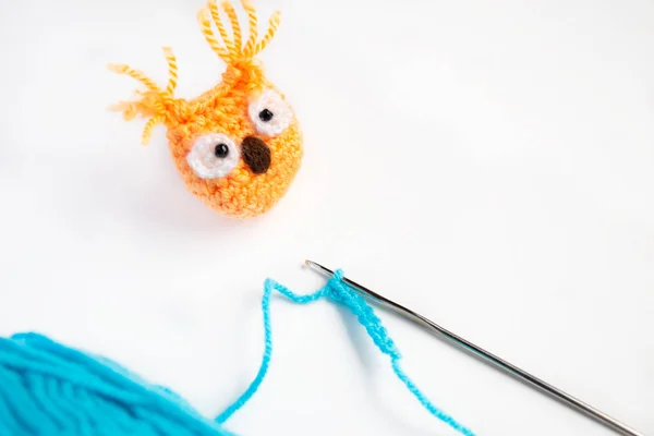 On a white background crochet, thread and a bound owl are contrasting, orange in color. Crocheting an owl. Crochet toys - knitting.