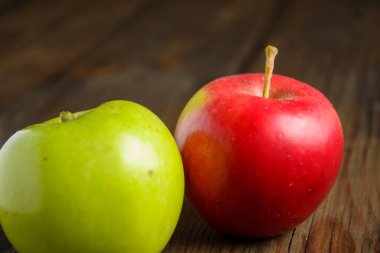Kırmızı ve yeşil elmalar ahşap bir masanın üzerinde yatar. Masada iki elma var. Yeşil ve kırmızı elmalar. Masada sağlıklı elmalar var..