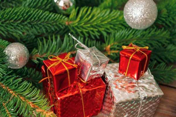 New Year's gifts next to the Christmas tree. On the wooden table are gifts with a Christmas tree. Decorated fir tree and Christmas gifts of white and red color.