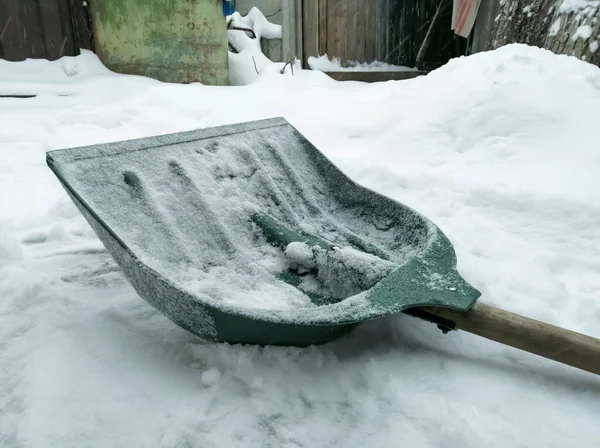 Shovel for snow outside. A green shovel for snow removal lies on a winter road. Snow with shovel for cleaning.