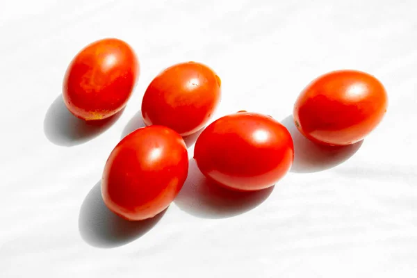 Cherry tomatoes on a white background. Five red tomatoes on a white background. Bright photo of tomatoes on white with a contrasting shadow.