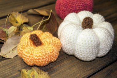 Örgü kabaklar düşmüş yaprakların arasında masanın üzerinde duruyor. Ev için sonbahar dekoru - kabak ve yapraklar örülmüş.