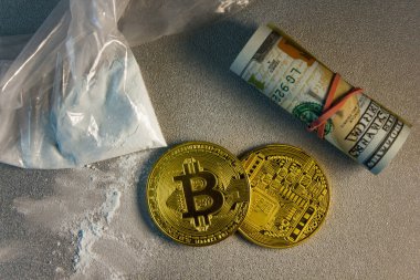 Beyaz tozlu şeffaf paket, iki Bitcoin sikke ve gri bir yüzey üzerinde dolar rulo